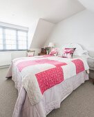 Pink and white quilt on bed below gable ceiling