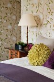 Green flower-shaped scatter cushion on bed against floral wallpaper