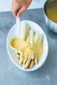 Sauce Hollandaise über weissen Spargel geben