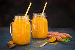 Karotten-Kurkuma-Smoothie in zwei Gläsern mit Trinkhalm