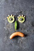 Symbolbild für versteckte Kohlenhydrate - trauriger Smiley aus Obst, Gemüse und Wurst