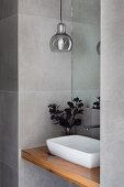 Countertop basin on wooden plate, pendant lamp in wall niche above in gray-tiled guest toilet