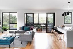 Elegant, open living room with gray and blue upholstered furniture, counter with bar stools, balcony in the background