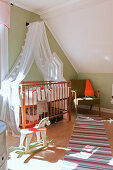 Cot with canopy in vintage-style nursery with green walls