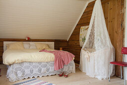 Cot under lace canopy next to double bed below sloping ceiling