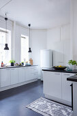 Black pendant lamps in front of windows in white fitted kitchen