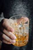 A hand holding a glass with an old fashioned cocktail