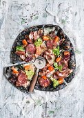 Black pizza with ham, sausage, bacon and vegetables