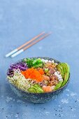 A Poke bowl with wakame seaweed, tuna, sushi rice, salmon, alfalfa sprouts, red cabbage, sesame seeds, cucumber slices, spring onions, avocado, and tobiko