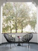 Two black Acapulco chairs and small side table on balcony with view of trees