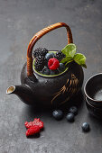 Teekanne mit frischen Beeren und Teeblättern