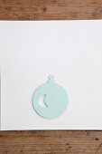 Christmas-tree bauble cut out of pale blue paper on white surface