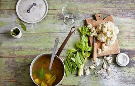 Spring vegetable stock in a pan with sugar snap peas, celery and cauliflower next to it