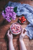 Woman eating strawberry banana ice cream in a bowl topped with goji berries and cacao nibs