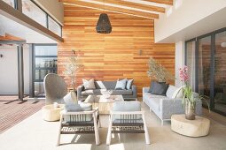 Designer furniture in shades of grey and wood-clad wall on veranda