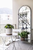 Bistro table and chairs in front of large wall-mounted mirror on balcony