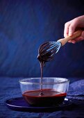 Chocolate sauce dripping from a whisk into a glass bowl