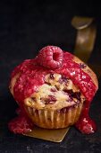 A raspberry muffin garnished with raspberry sauce and a single raspberry (close up)