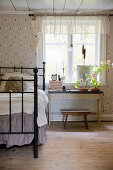 Metal bed next to window in bedroom with vintage-style wallpaper