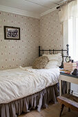 Metal bed with valance in bedroom with vintage-style wallpaper