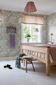 Wooden bench at foot of bed in bedroom with floral wallpaper