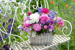 Korb mit Fruehsommergesteck aus Stauden auf Gartenbank :