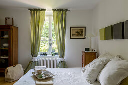 Breakfast tray on double bed and antique bedside cabinet in rustic bedroom with green curtains