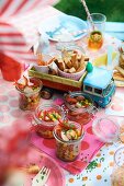 Red pepper and sweetcorn salad with sausages in glass jars and breadsticks for a children's party in the garden