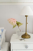 Lamp and sprig of flowers on white bedside cabinet