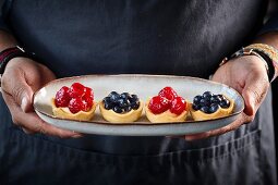 Various berry tarts on an oval dish