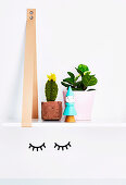 Hanging shelf with crochet cactus and houseplant above the wall sticker