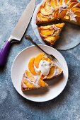 A peach cake with two slices cut out and served on a plate with cream