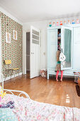 Girl in front of mint-green wardrobe with mirrored door in child's bedroom with retro wallpaper