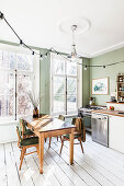 Green wall, white wooden floor and dining set in front of large windows in kitchen-dining room