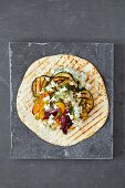 A tortilla wrap with grilled vegetables, feta and tzatziki