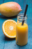 A mango and orange smoothie in a bottle with a straw