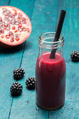 A blackberry and pomegranate smoothie in a bottle with a straw