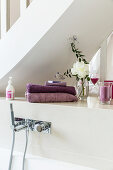 Towels, flowers and scented candle on shelf above wall-mounted bath taps