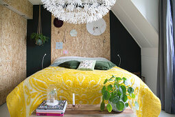 Yellow felt blanket on bed in bedroom with chipboard panels on walls