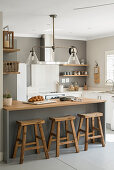 Counter with wooden barstools in open-plan renovated kitchen with grey wall