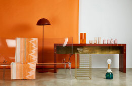Transparent designer sofa, standard lamp and vases on console table against orange wall