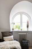 Cushions and sheepskin on bed next to arched window