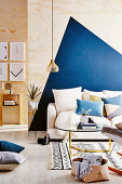 Couch with cushions and coffee table in front of plywood wall with a blue, geometric pattern