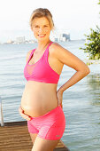 A pregnant woman on a jetty wearing a pink sports bra and shorts