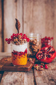 Parfait in a glass with mango pureé, pomegranate seeds, coconut yoghurt and redcurrants