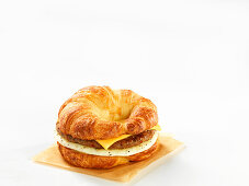 Ein Croissant-Burger mit Käse und Ei vor weißem Hintergrund