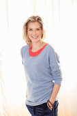 A young blonde woman wearing a blue jumper over a red top