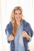 A young blonde woman wearing a denim shirt with a jumper over her shoulders