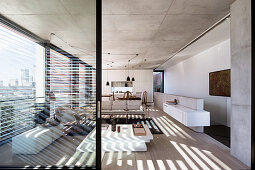 View into open living room with designer furniture, window front and concrete ceiling