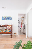 Colourful cushions on wooden bench below colourful painting on living room wall